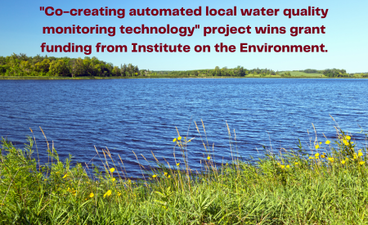 A photograph of a Minnesota lake on a sunny summer day. The sky is clear, the water is a deep blue, and wildflowers and grasses are in the foreground. At the top of the image, maroon text reads, "'Co-creating automated local water quality monitoring technology' project wins grant funding from Institute on the Environment."