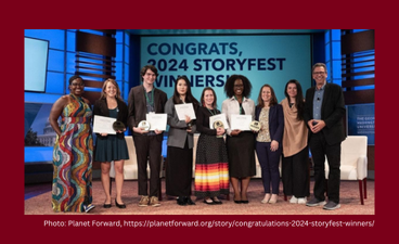 A group of eight college and graduate students of different ethnicities stand on a stage in a line holding certificates. Behind them is a screen that reads, "Congrats, 2024 Storyfest winners!" In the center of the line of people is Mickki Garrity, a woman wearing a black polka-dotted ribbon skirt who is attending U of M. At the far right stands a light-skinned man in a dark suit. He is wearing a microphone on his lapel and appears to be a discussion monitor.