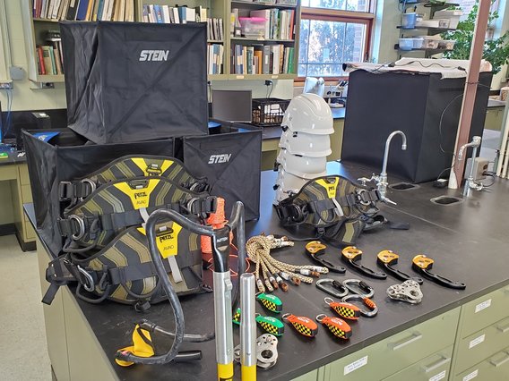 Photo of tree climbing equipment laid out on a lab table. Equipment includes climbing harnesses, ropes, carabiners, and more.