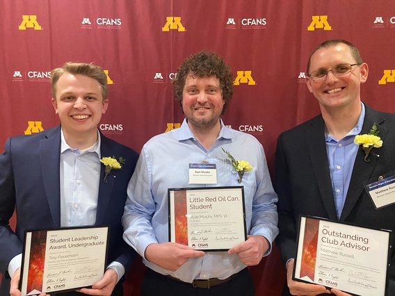 photo of Trey Feurhelm (a young white man in a blue suit), Ryan Murphy (a white man in a blue shirt)), and Matt Russell (a white man in a dark blue suit) receiving awards in front of a maroon background