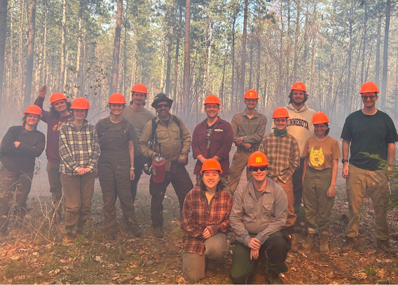 A group of 13 students and a fire manager pose near the controlled burn.