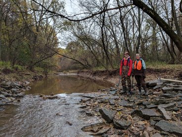 Two researchers in waders pose near Plum Creek at a study site