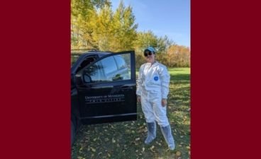Diana Karwan in field gear next to a black SUV with the University of Minnesota logo on the driver's side door.