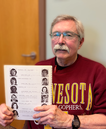 Steve Cook holds a copy of his 1975 college yearbook in his hands, which is turned to his senior portrait.