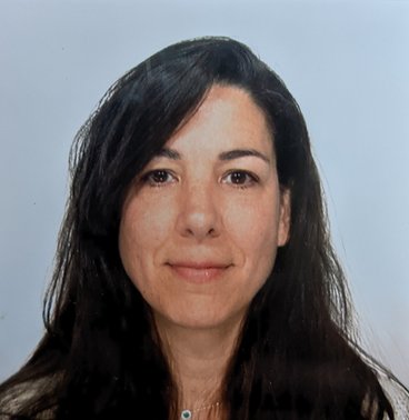 A Caucasian woman with long, straight brown hair and brown eyes smiles in front of a neutral background.