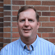 photo of Dr. Mike Kilgore, professor and head of the department of forest resources. White man in blue shirt smiling against a brick background.