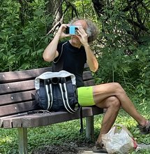 photo of a man with grey hair sitting on a park bench and looking through a pair of augmented reality goggles